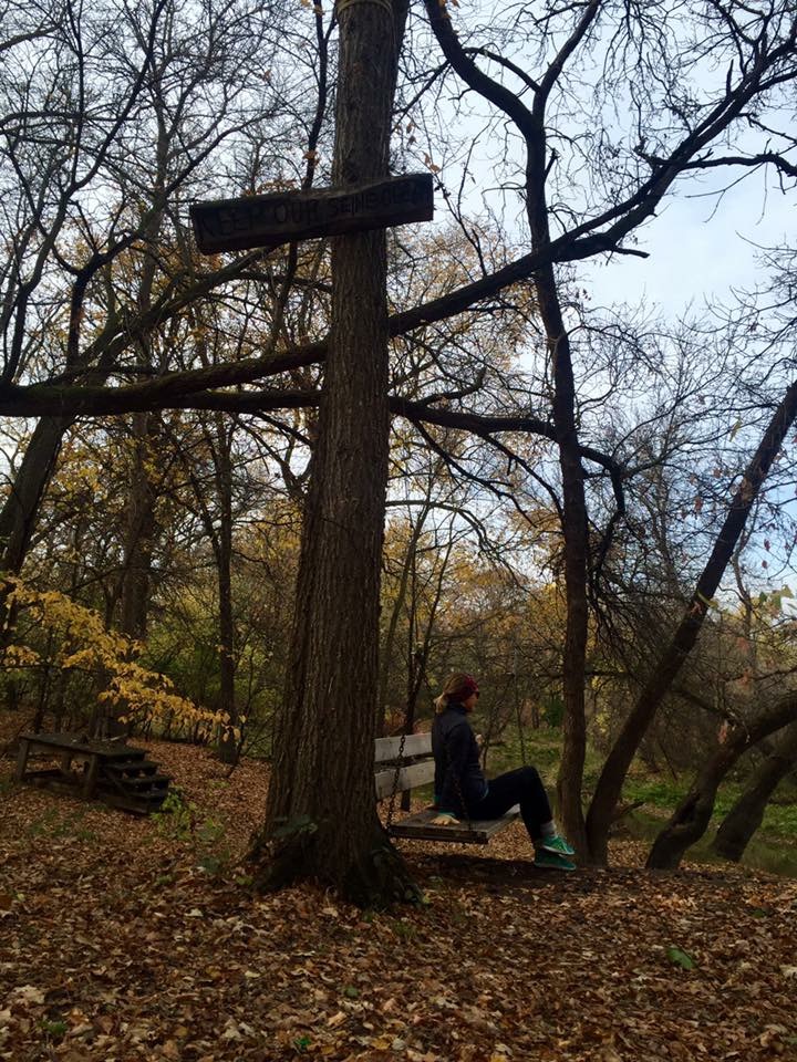 Image of a person sitting on a bench swing in the forest.